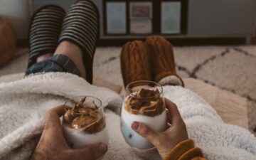 Image of a man and a woman holding two glasses while snuggled under a blanket 3 - Rendé