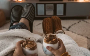 Image of a man and a woman holding two glasses while snuggled under a blanket 1 - Rendé