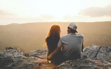 Man and women sitting close to each other on cliff at sunset