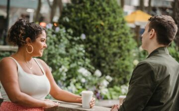 Man and woman standing near wall with take away coffee cups