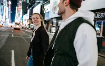 Man and women walking through a city at night and looking at each other while smiling.