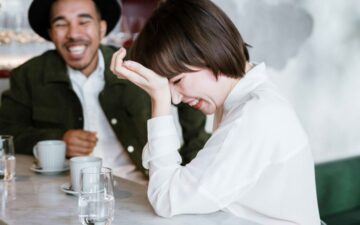 Female laughing with head in hand and man in the background.